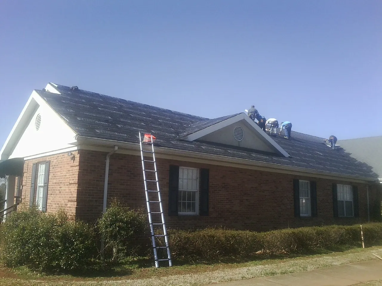 Crew tearing shingles off a brick ranch roof with a ladder set — Emergency Roof Repair work by our crew in Fryeburg