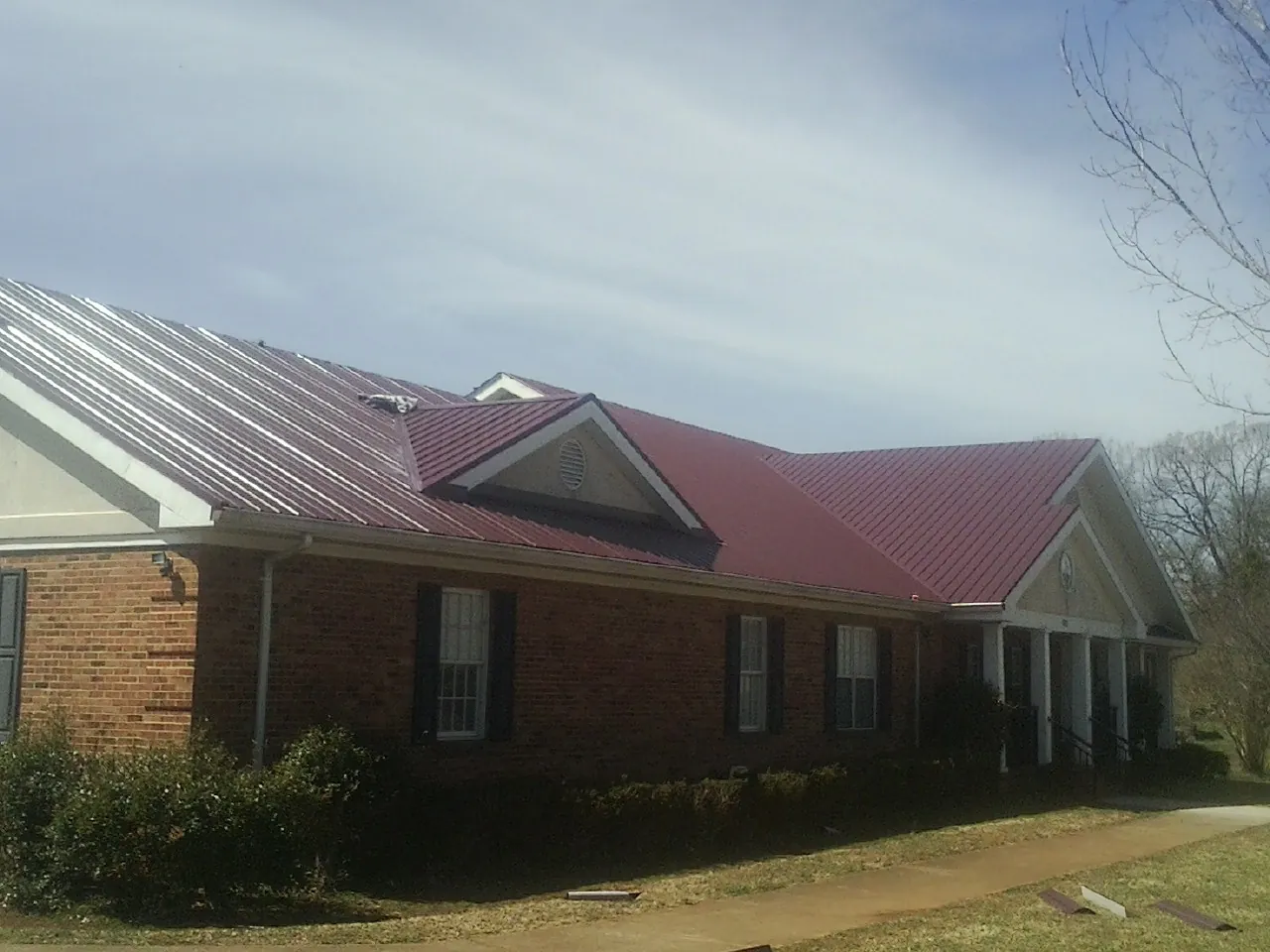Red metal roof with gabled entries on a long brick building, from a Hail Damage Roof Repair job in Fryeburg