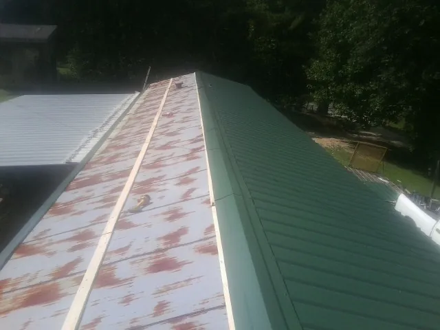 Old rusted panels beside newly installed green metal roofing — Wind Damage Roof Repair by Roofing Brothers in Fryeburg