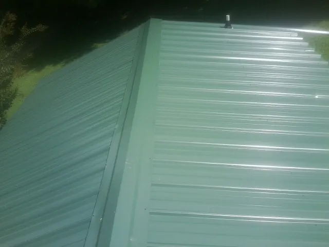 New green metal panels meeting at the ridge of a roof — Flat Roof Repair work by our crew in Fryeburg