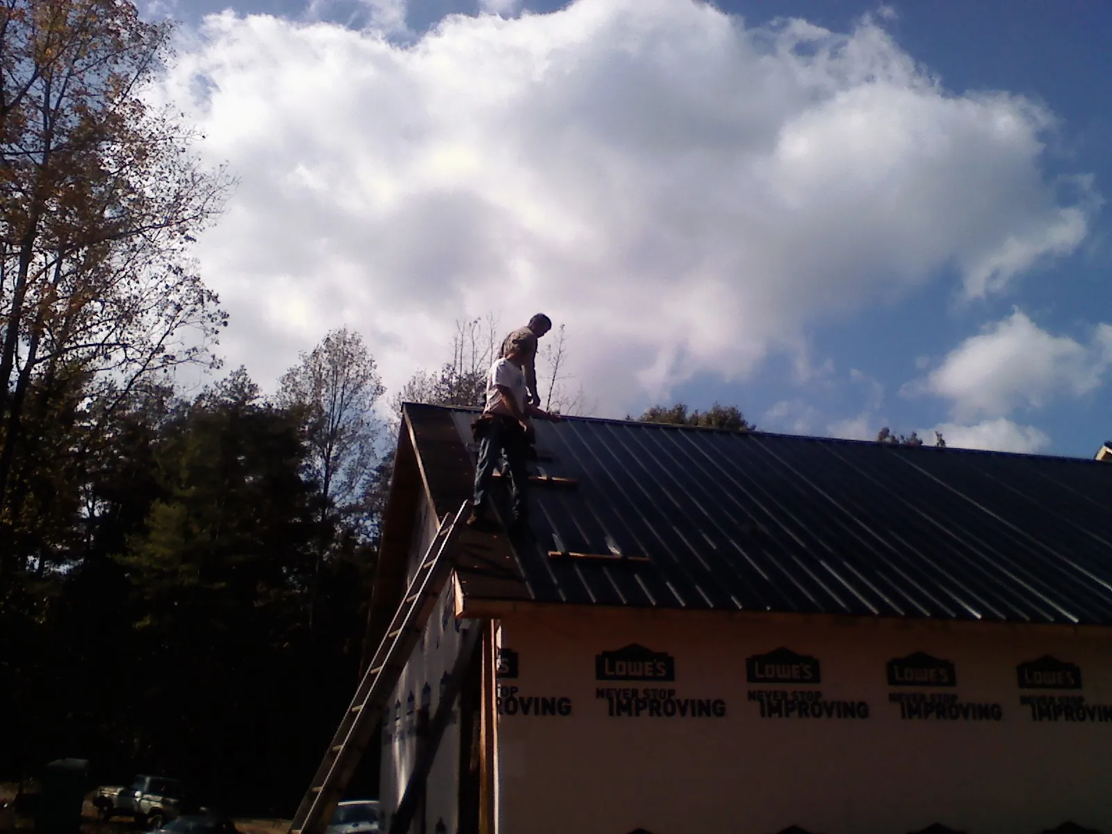 Roofer fastening dark metal panels high against a cloudy sky, from a Roof Inspection job in Fryeburg