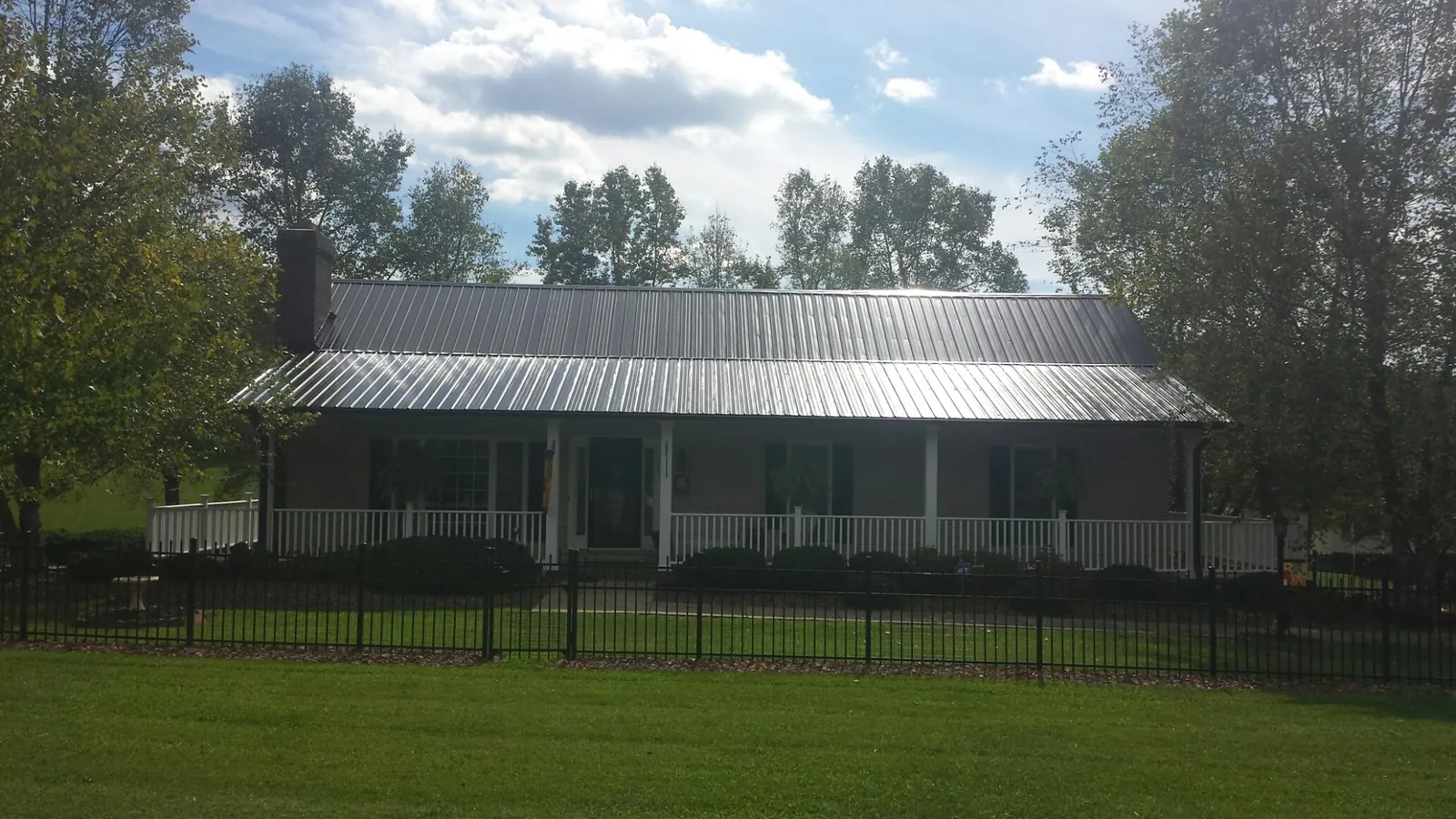 Gray metal roof on a brick ranch with a full width front porch — Gutter Guard Installation work by our crew in Fryeburg