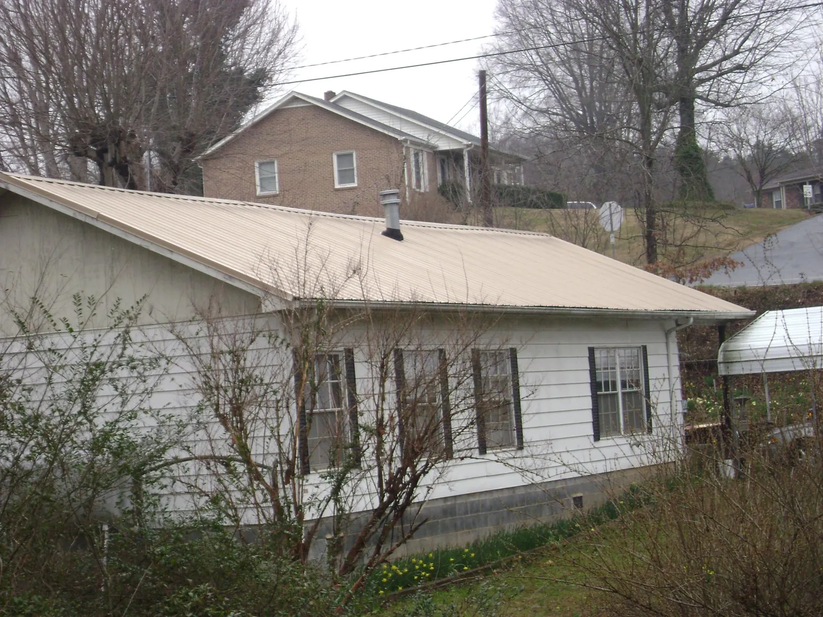 Tan metal roof on a white sided house set into a hillside — Commercial Roofing by Roofing Brothers in Fryeburg