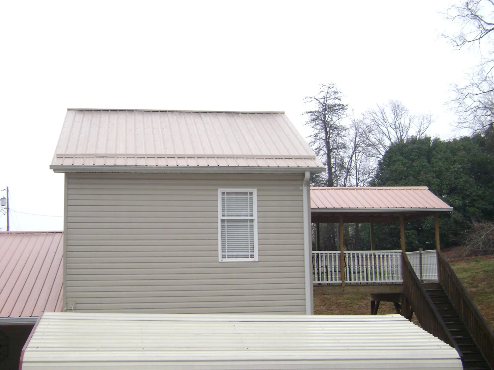 Tan metal roofs on a two story addition and attached porch, from a Roof Replacement job in Fryeburg
